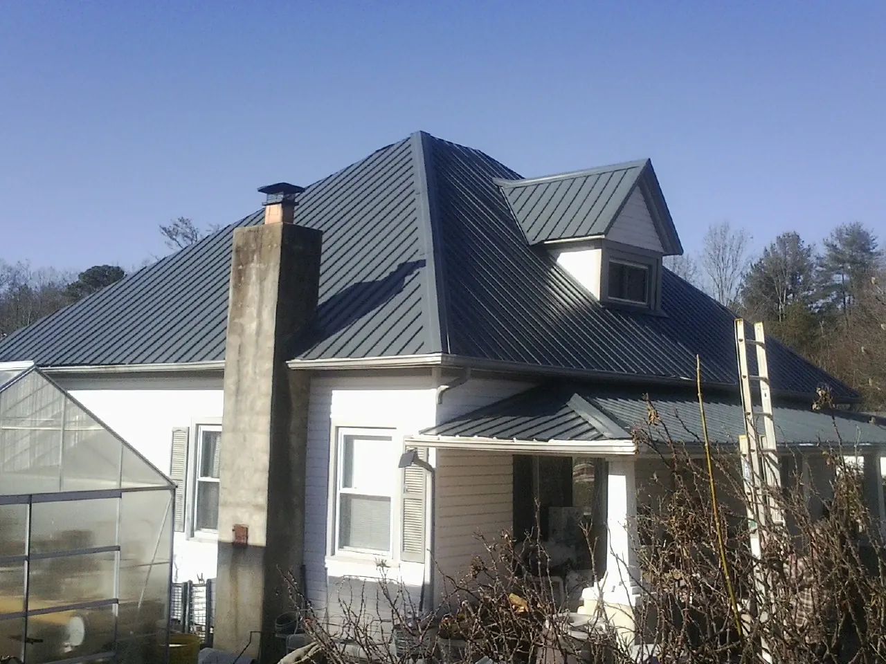 Dark blue standing seam metal roof on a white farmhouse with dormer — Slate & Tile Roof Repair by Roofing Brothers in Zion