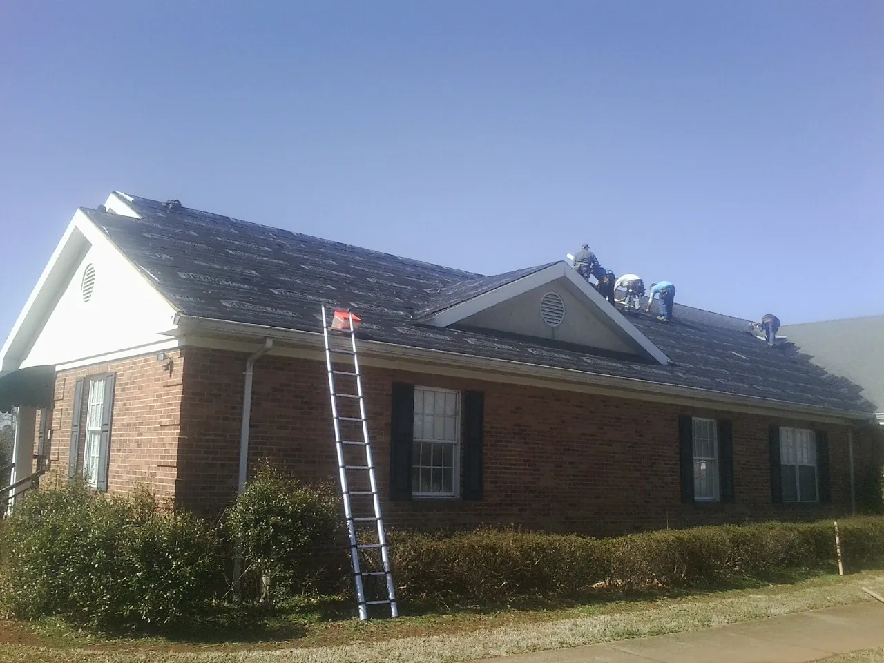 Crew tearing shingles off a brick ranch roof with a ladder set — Emergency Roof Repair work by our crew in Zion
