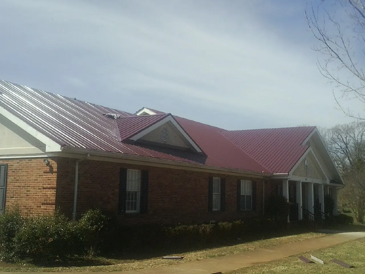 Red metal roof with gabled entries on a long brick building, from a Hail Damage Roof Repair job in Zion