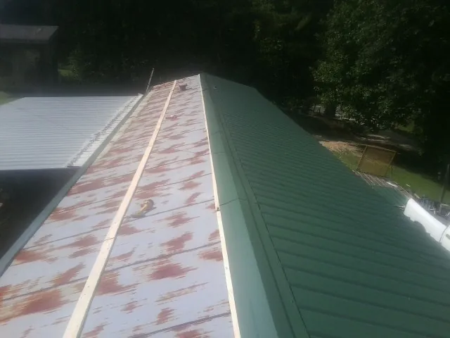 Old rusted panels beside newly installed green metal roofing — Wind Damage Roof Repair by Roofing Brothers in Zion