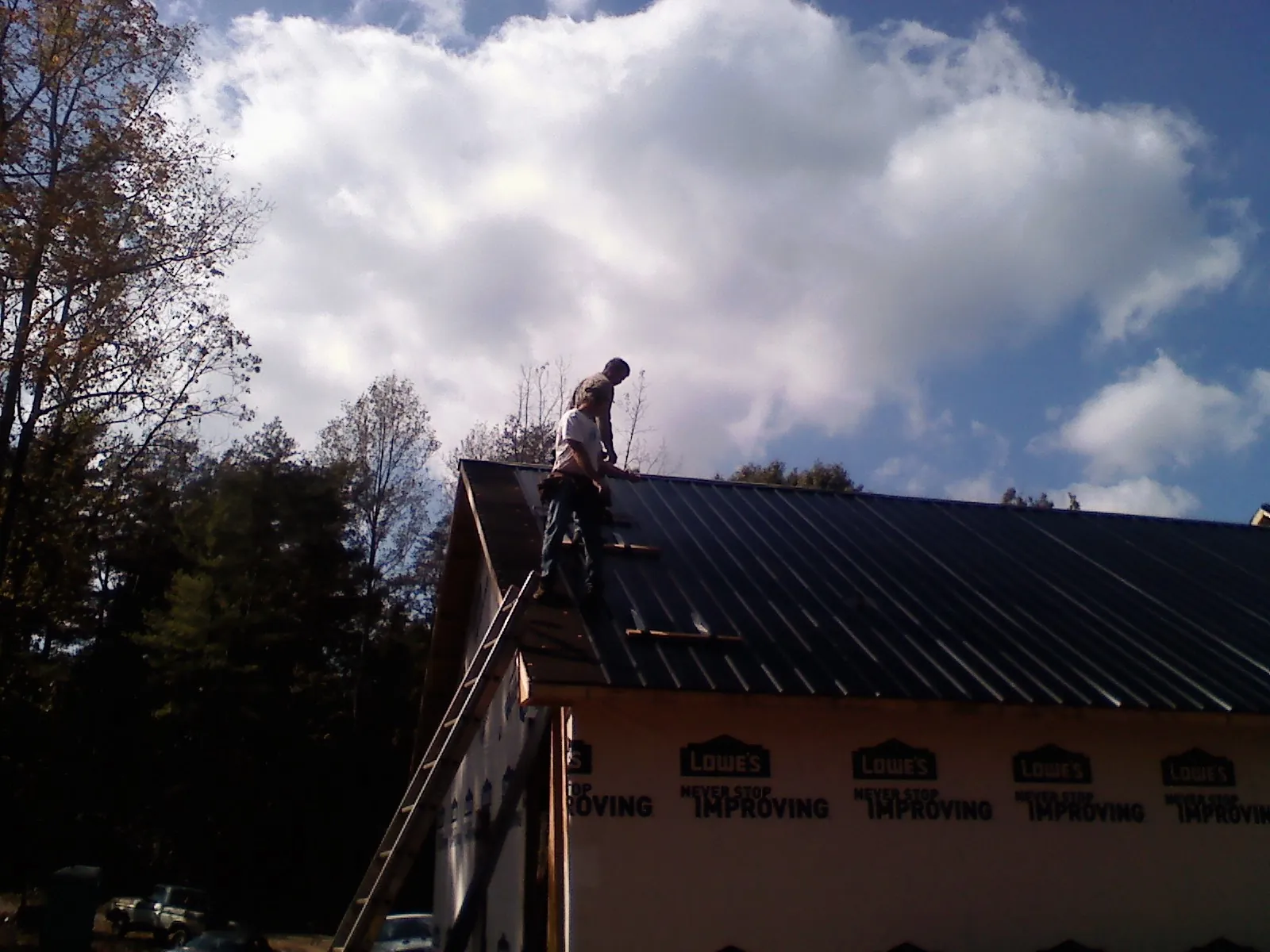 Roofer fastening dark metal panels high against a cloudy sky, from a Roof Inspection job in Zion