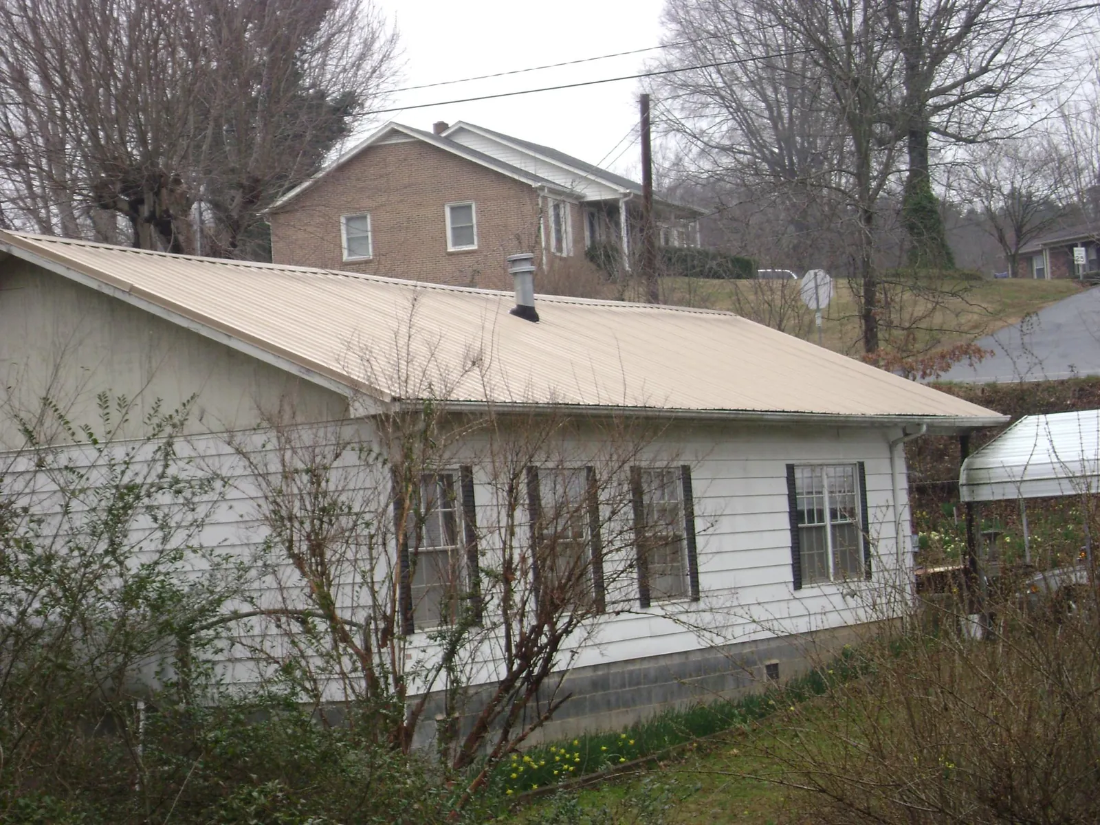 Tan metal roof on a white sided house set into a hillside — Commercial Roofing by Roofing Brothers in Zion